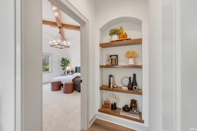 hall featuring beamed ceiling, carpet floors, built in features, and a notable chandelier