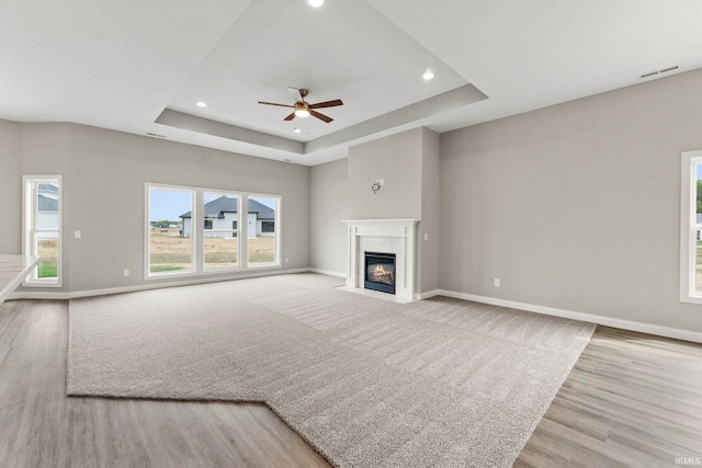 unfurnished living room featuring a raised ceiling, ceiling fan, a high end fireplace, and light hardwood / wood-style flooring