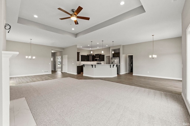 unfurnished living room featuring a raised ceiling, ceiling fan with notable chandelier, and dark hardwood / wood-style flooring