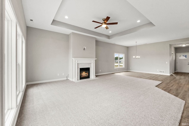 unfurnished living room featuring hardwood / wood-style floors, ceiling fan with notable chandelier, a high end fireplace, and a tray ceiling