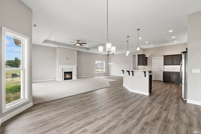 unfurnished living room featuring ceiling fan with notable chandelier, hardwood / wood-style floors, and a tray ceiling