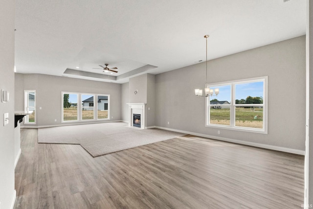 unfurnished living room featuring light hardwood / wood-style flooring, a tray ceiling, ceiling fan with notable chandelier, and a healthy amount of sunlight