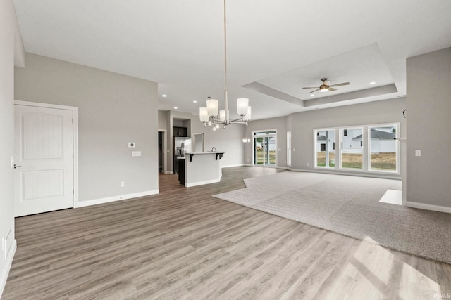 unfurnished living room featuring hardwood / wood-style flooring, ceiling fan with notable chandelier, and a tray ceiling