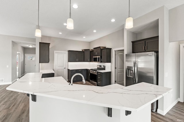 kitchen featuring stainless steel appliances, a kitchen breakfast bar, wood-type flooring, light stone countertops, and decorative light fixtures