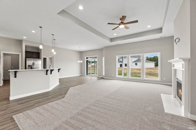 living room with ceiling fan, a healthy amount of sunlight, dark hardwood / wood-style floors, and a raised ceiling