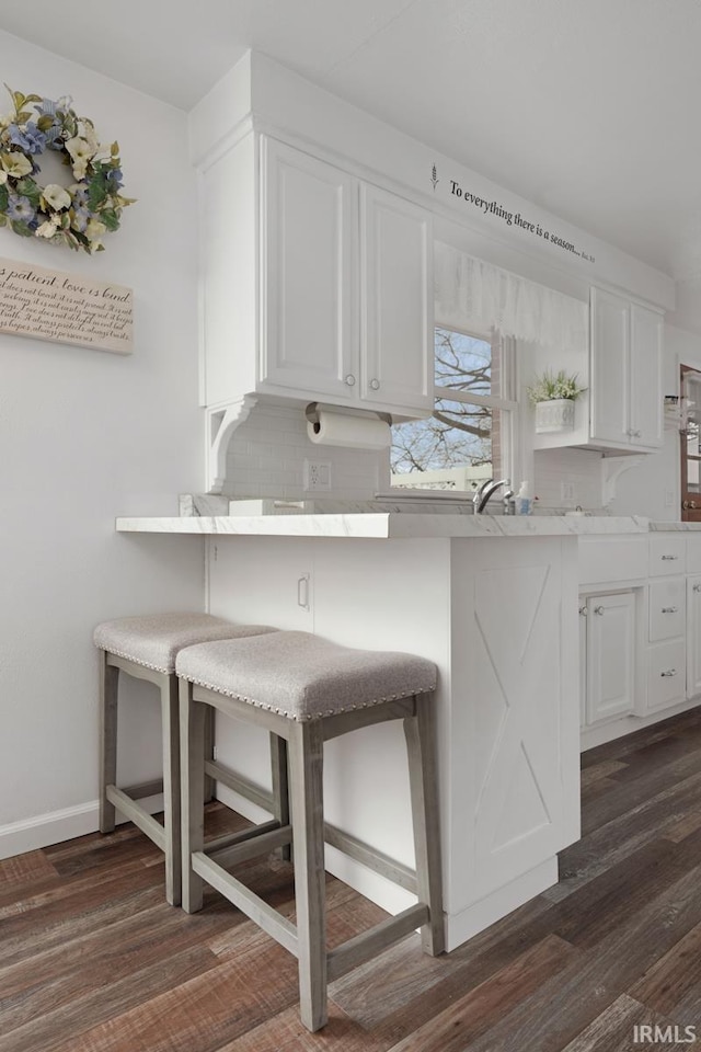 kitchen featuring dark wood-type flooring, a breakfast bar, kitchen peninsula, and white cabinets