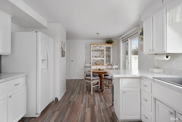 kitchen featuring dark wood-type flooring, white cabinetry, white refrigerator with ice dispenser, decorative light fixtures, and kitchen peninsula