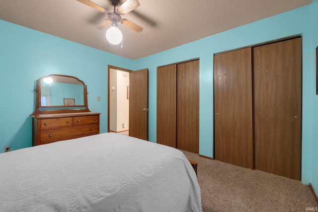 carpeted bedroom with two closets, a textured ceiling, and ceiling fan