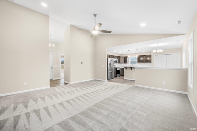 unfurnished living room with high vaulted ceiling, ceiling fan with notable chandelier, and light colored carpet