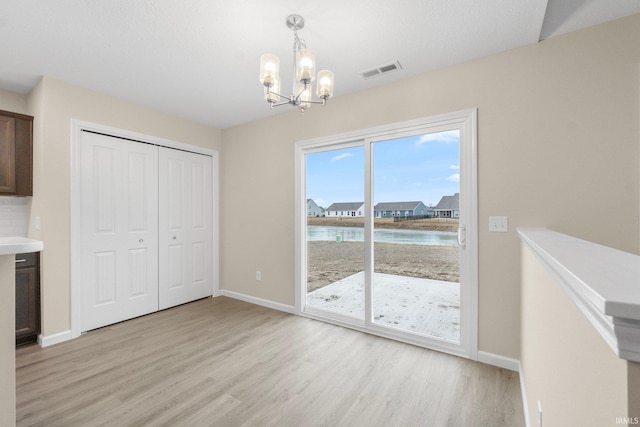 unfurnished dining area with a water view, a chandelier, and light wood-type flooring