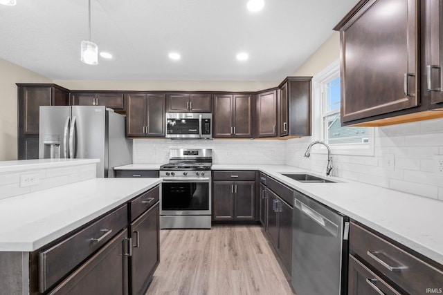 kitchen with pendant lighting, sink, stainless steel appliances, dark brown cabinetry, and light hardwood / wood-style floors