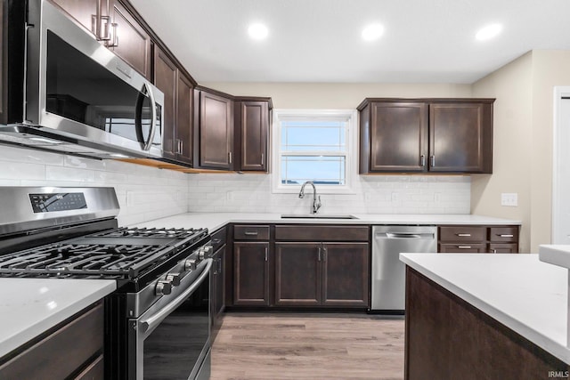 kitchen featuring sink, dark brown cabinets, light hardwood / wood-style flooring, stainless steel appliances, and decorative backsplash