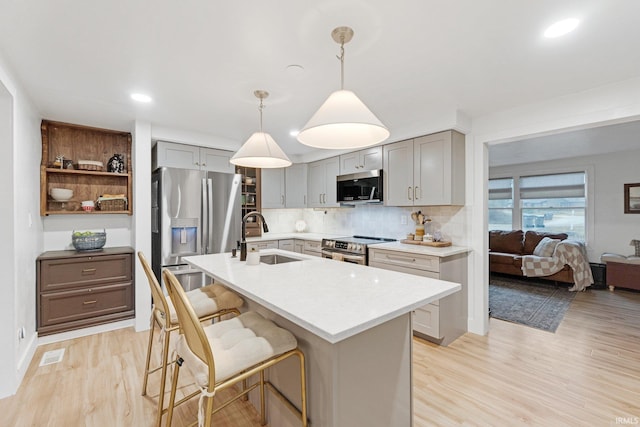 kitchen with a kitchen island with sink, sink, stainless steel appliances, and hanging light fixtures