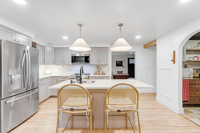 kitchen featuring decorative light fixtures, a breakfast bar area, stainless steel appliances, and a center island with sink