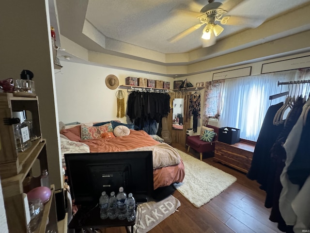 bedroom featuring dark hardwood / wood-style flooring, ceiling fan, a raised ceiling, and a textured ceiling