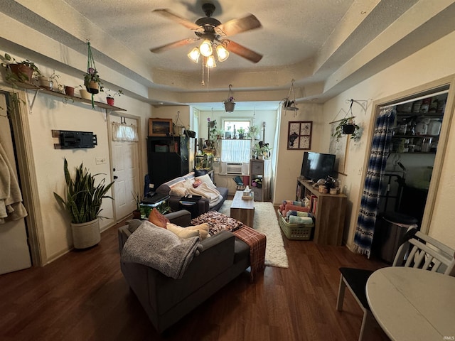 living room featuring ceiling fan, a textured ceiling, dark hardwood / wood-style flooring, and a tray ceiling