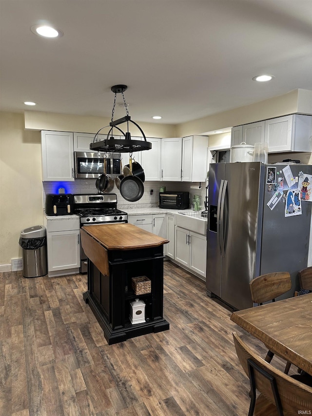 kitchen featuring dark wood-type flooring, appliances with stainless steel finishes, hanging light fixtures, and white cabinets