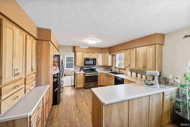 kitchen featuring black appliances, sink, kitchen peninsula, light brown cabinets, and light wood-type flooring