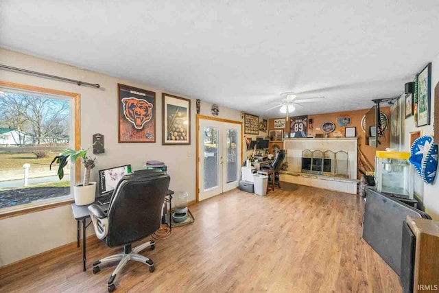 office space featuring a tiled fireplace, hardwood / wood-style flooring, ceiling fan, and french doors