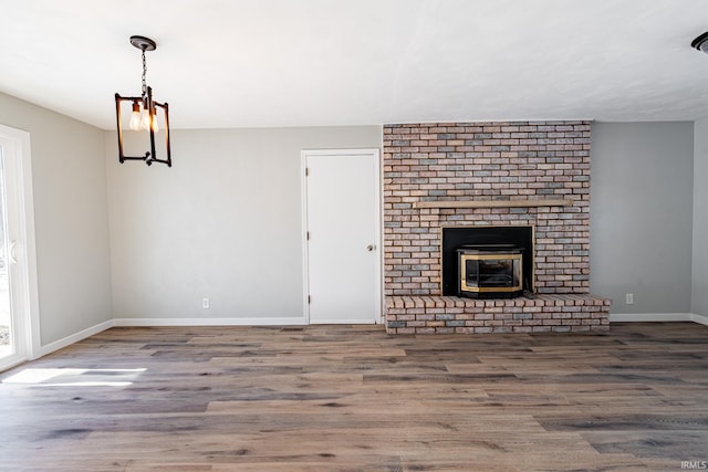 unfurnished living room with a fireplace, a notable chandelier, and wood-type flooring