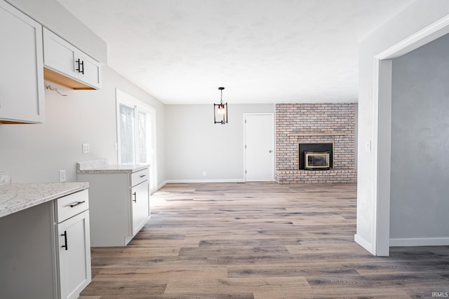 kitchen featuring light hardwood / wood-style flooring, hanging light fixtures, light stone countertops, white cabinets, and a brick fireplace