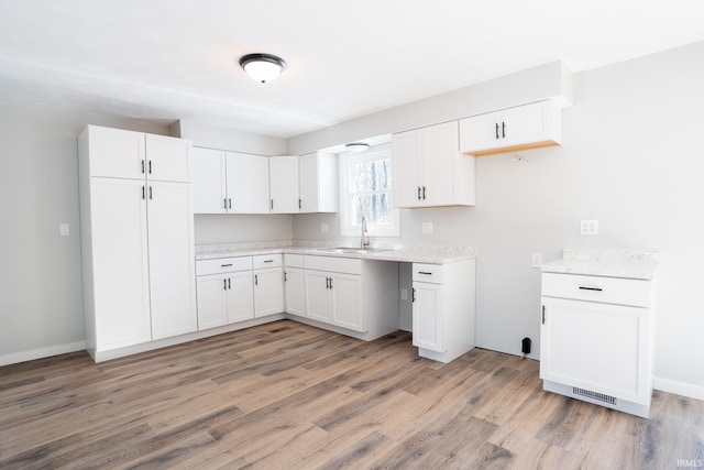 kitchen featuring white cabinetry, sink, light stone counters, and light hardwood / wood-style flooring