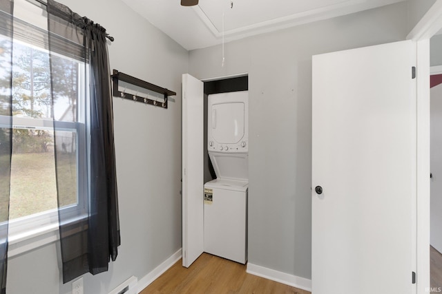 washroom with stacked washer and dryer, baseboard heating, ceiling fan, and light hardwood / wood-style flooring