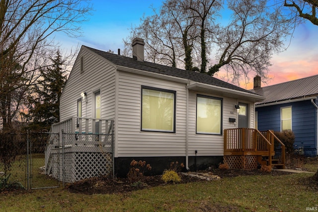 back house at dusk featuring a lawn and a deck