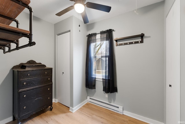 bedroom with ceiling fan, a baseboard heating unit, and light hardwood / wood-style floors