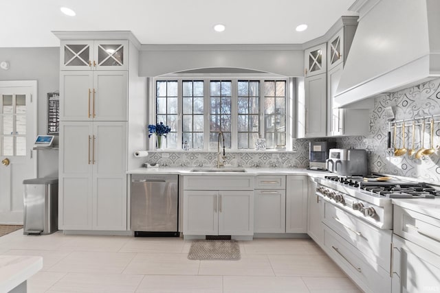 kitchen with gray cabinets, appliances with stainless steel finishes, tasteful backsplash, sink, and custom range hood