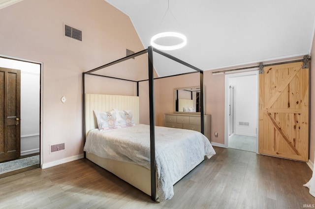 bedroom featuring hardwood / wood-style flooring, vaulted ceiling, and a barn door