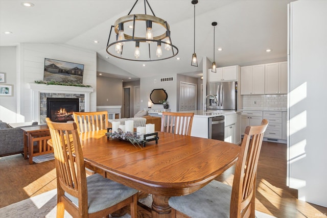 dining room with dark wood-type flooring, an inviting chandelier, a fireplace, and vaulted ceiling