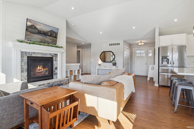 living room with dark hardwood / wood-style flooring, a stone fireplace, and vaulted ceiling