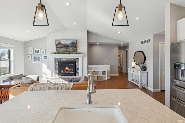 kitchen featuring a stone fireplace, sink, decorative light fixtures, stainless steel fridge, and light stone countertops