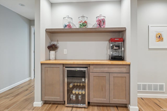 bar with wine cooler and light hardwood / wood-style flooring