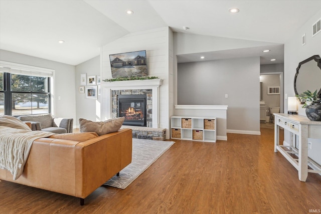 living room with lofted ceiling, hardwood / wood-style floors, and a stone fireplace