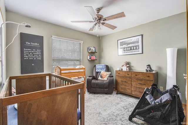 bedroom with light carpet, a nursery area, and ceiling fan