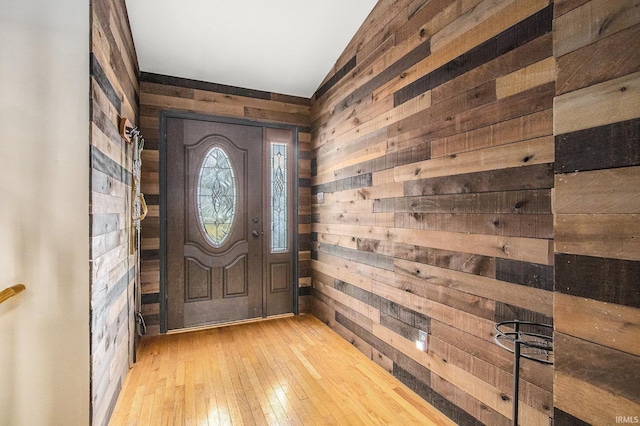 foyer with light wood-type flooring, vaulted ceiling, and wood walls