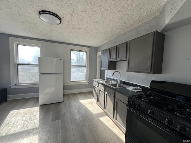 kitchen with sink, a textured ceiling, black gas range oven, white fridge, and light hardwood / wood-style floors