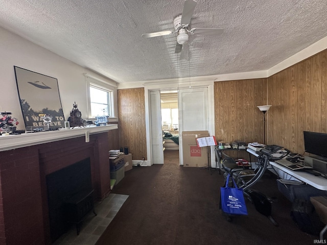 office area featuring ceiling fan, a textured ceiling, dark carpet, and wood walls