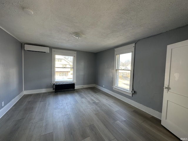 unfurnished room featuring radiator, a wall mounted air conditioner, wood-type flooring, and a healthy amount of sunlight