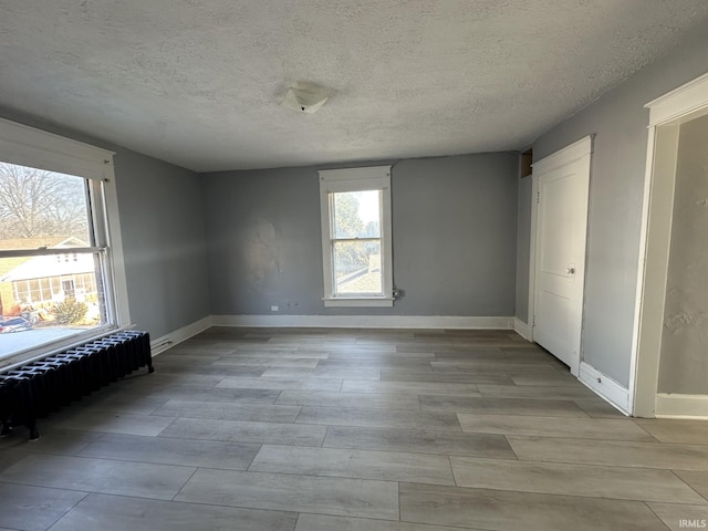 empty room featuring radiator heating unit, light hardwood / wood-style floors, and a textured ceiling