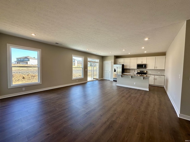 kitchen with white cabinetry, stainless steel appliances, tasteful backsplash, a center island with sink, and dark hardwood / wood-style flooring