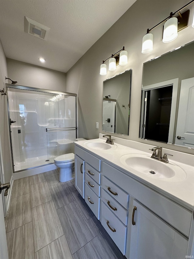 bathroom featuring walk in shower, vanity, toilet, and a textured ceiling