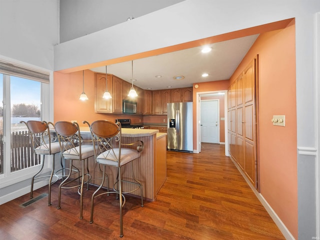 kitchen with a breakfast bar, decorative light fixtures, dark hardwood / wood-style flooring, kitchen peninsula, and stainless steel appliances