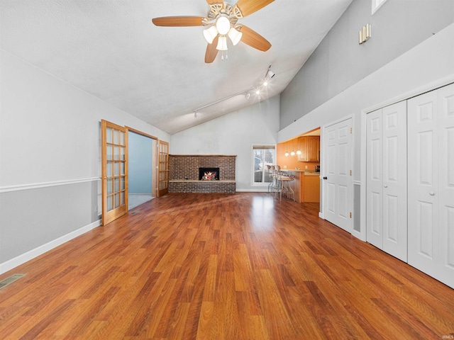 unfurnished living room featuring high vaulted ceiling, a fireplace, light hardwood / wood-style floors, and ceiling fan