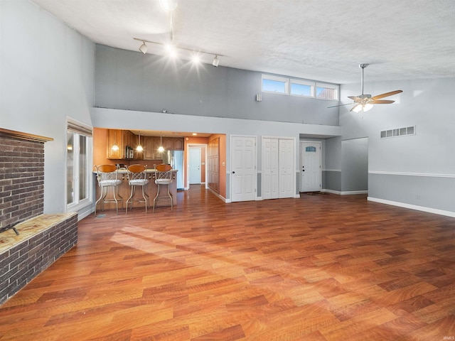 unfurnished living room with ceiling fan, light hardwood / wood-style floors, a textured ceiling, and a high ceiling