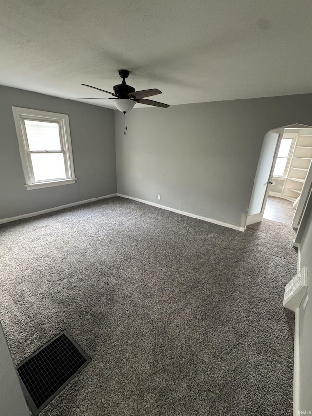 empty room featuring ceiling fan, a textured ceiling, and dark carpet