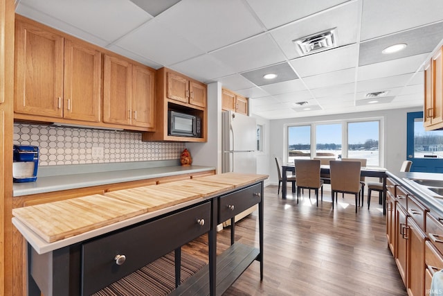 kitchen featuring dark wood-type flooring, wooden counters, black microwave, white fridge, and backsplash