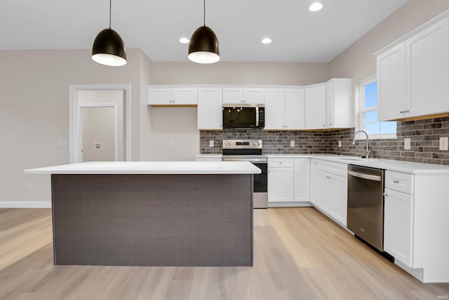 kitchen with hanging light fixtures, a kitchen island, white cabinets, and appliances with stainless steel finishes